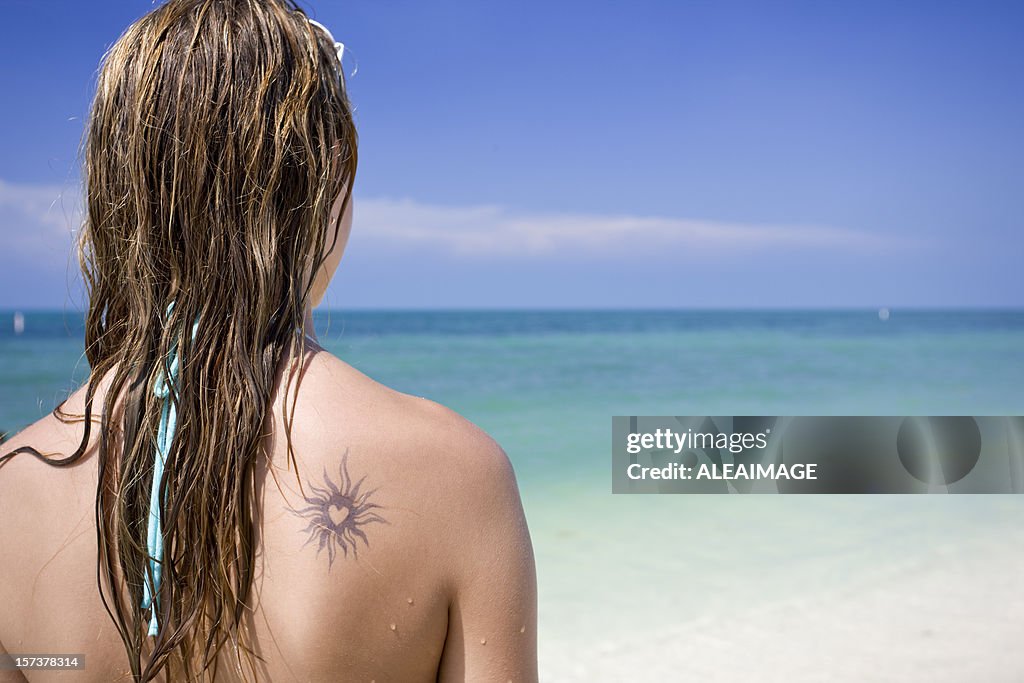 Mädchen, Blick auf das Meer mit tattoo auf dem Rücken.