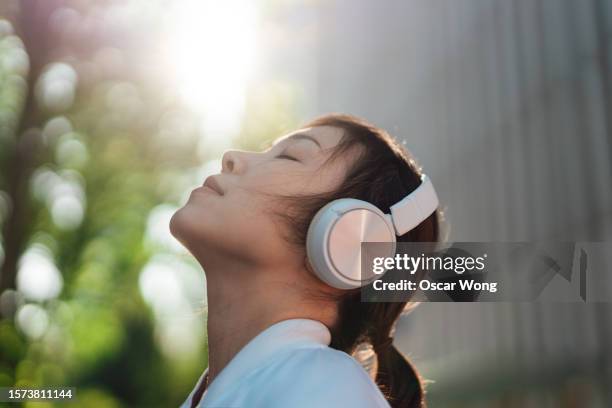 headshot of young asian woman with eyes closed, listening to music with wireless headphones - music therapy stock pictures, royalty-free photos & images
