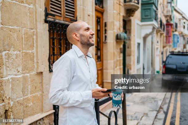 young man drinking coffee and using phone on the street in cospicua malta - malta business stock pictures, royalty-free photos & images