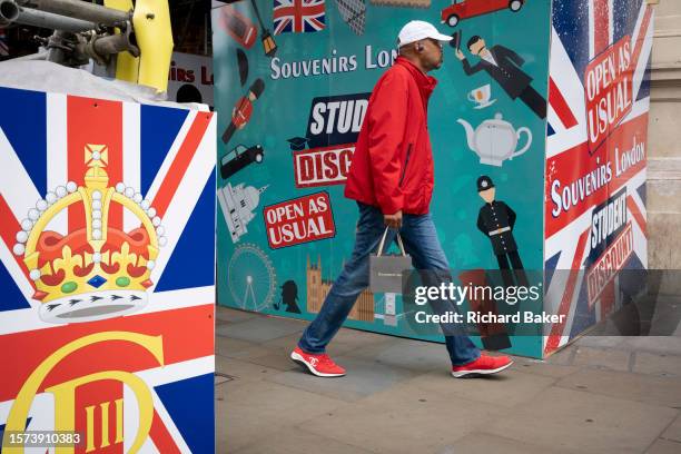 Man walks past tourist souvenir hoardings at Piccadilly Circus in the West End, on 25th July 2023, in London, England.