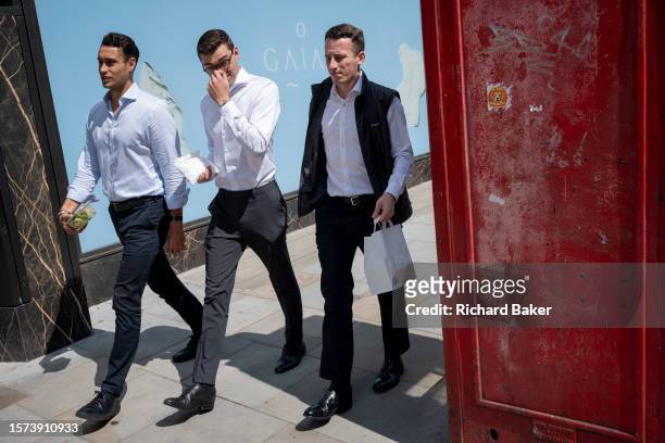 Work colleagues carry takeaway lunches and walk past a red phone box and blue hoarding for a forthcoming retail business on Piccadilly in the...