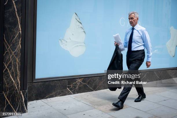 Businessman wearing a blue shirt walks past a matching blue hoarding for a forthcoming retail business on Piccadilly in the capital's West End, on...