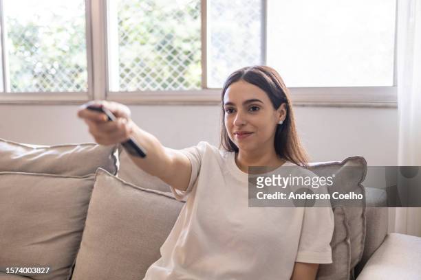 woman turning on the tv by remote control - disconnect filme imagens e fotografias de stock