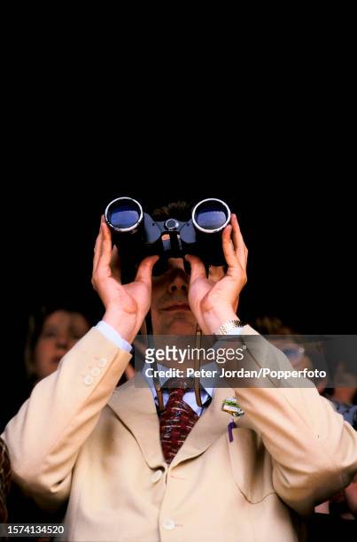 Punter uses a pair of binoculars to view the racing during the 1000 Guineas Stakes flat horse race meeting at Newmarket Racecourse in Suffolk,...