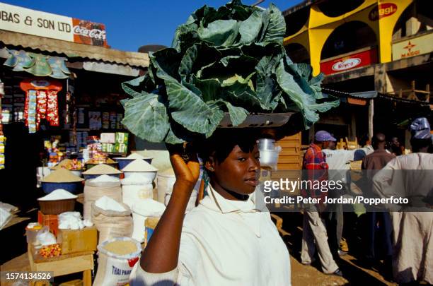 Woman carries a tray of cabbages on her head past market stalls at a street market in the city of Lagos in southern Nigeria in 2001.
