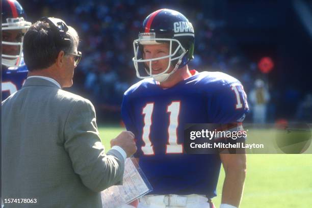 Phil Simms of the New York Giants talks to head coach Dan Reeves during a NFL football game against the Washington Redskins on October 10, 1993 at...