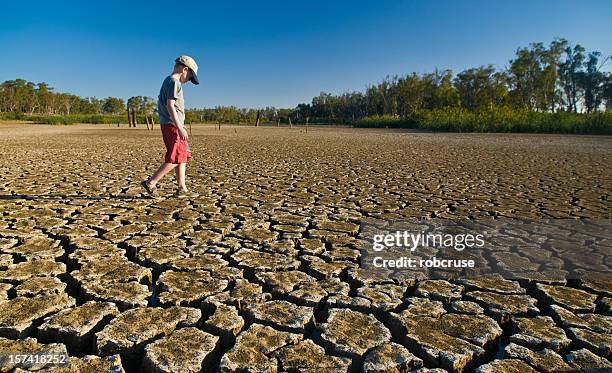 young boy walking on a dry lake bed looking down - värmebölja bildbanksfoton och bilder