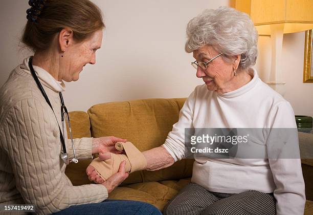 home healthcare professional wrapping wrist of senior woman - wrapping arm stock pictures, royalty-free photos & images