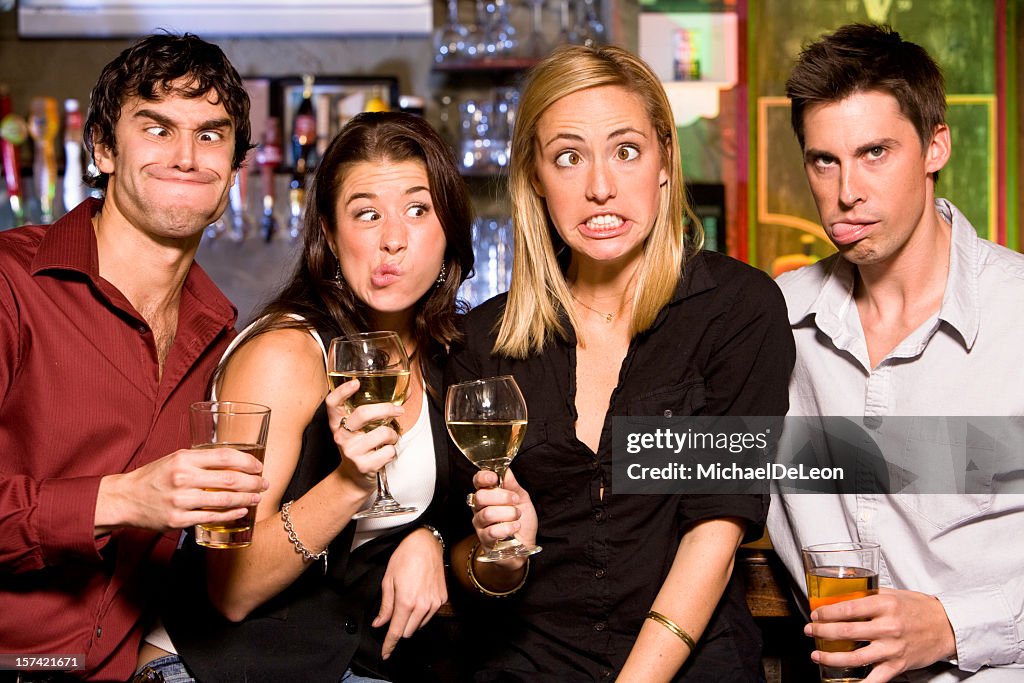 Four friends making funny faces at a bar with beer and wine