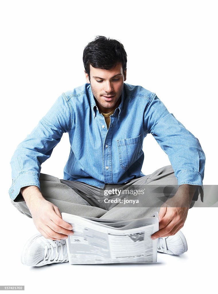 Young man sitting on the floor reading newspaper