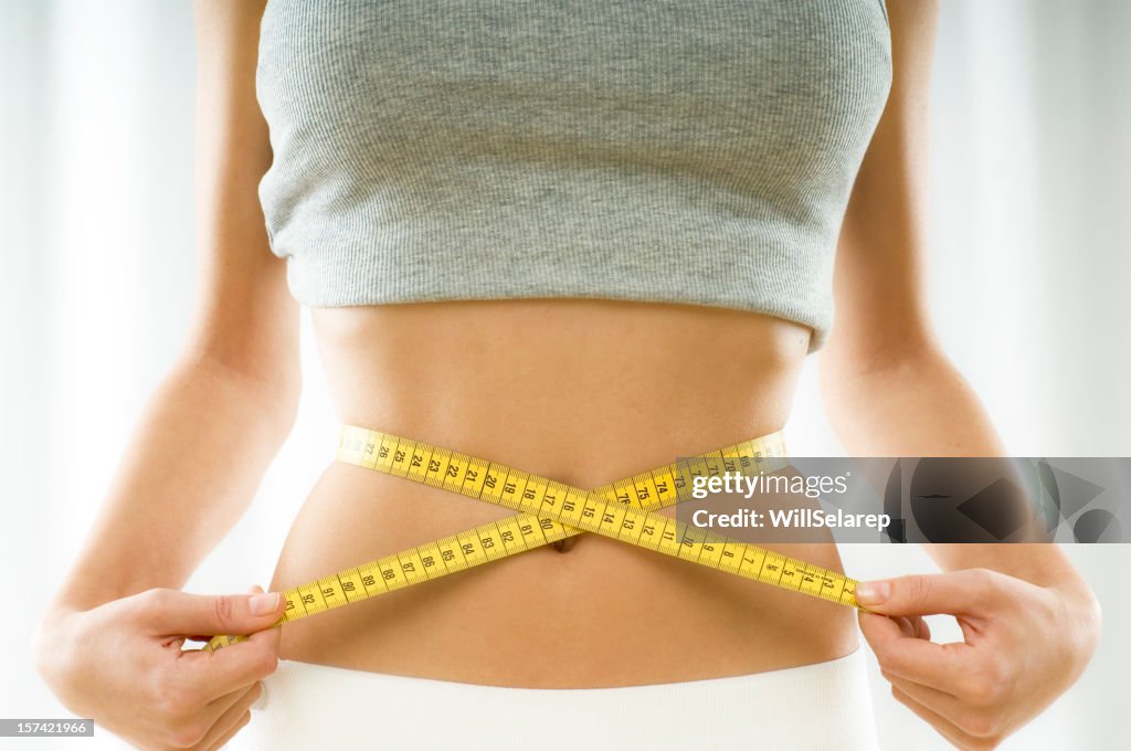 Mid section view of a young woman measuring her waist