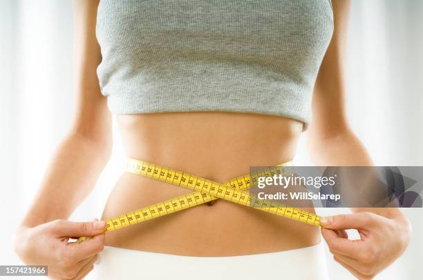 mid section view of a young woman measuring her waist - waist stockfoto's en -beelden