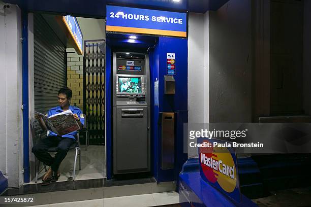 Man reads a newspaper beside a new ATM bank machine, on November 30, 2012 in downtown Yangon, Myanmar. Business opportunities are expanding in the...