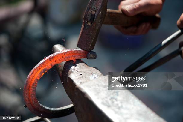 a man striking a red hot horseshoe on the anvil - hoefijzer stockfoto's en -beelden