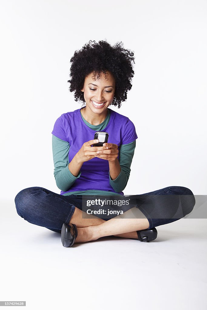 Pretty young woman sitting cross-legged texting smiling