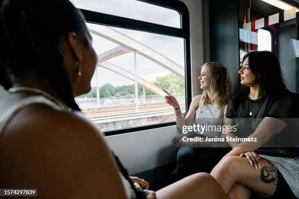 three young female friends sitting in a train next to a window - zug stock pictures, royalty-free photos & images