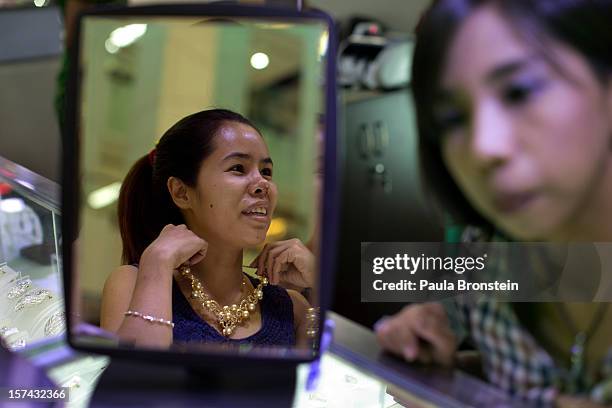 Woman tries on a gold and pearl necklace at the Junction Square shopping mall on November 30, 2012 in downtown Yangon, Myanmar. Business...