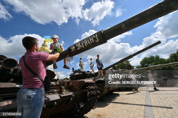 Man holds his son sitting on the barrel of a destroyed tank during an open-air exhibition of destroyed Russian military vehicles at Mykhaylo Square...