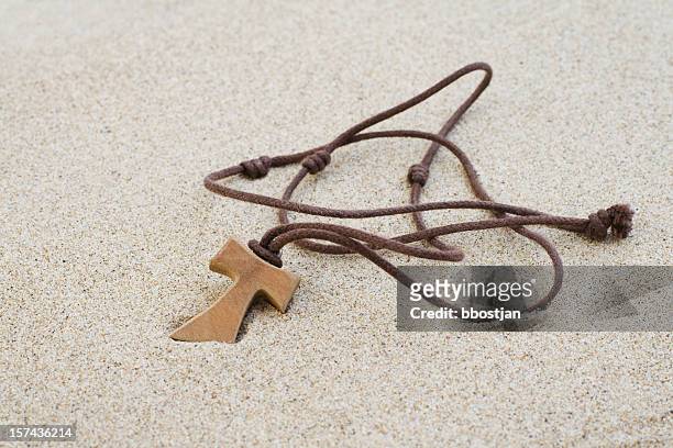 tau cross in den sand stecken - a cross necklace stock-fotos und bilder