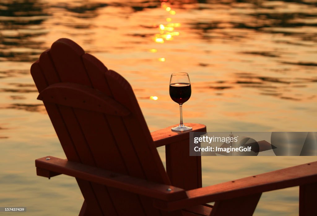 Adirondack-Stuhl und Wein bei Sonnenuntergang am See