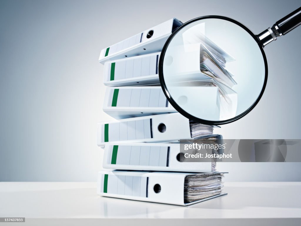 Pile of binders partially obscured by a magnifying glass