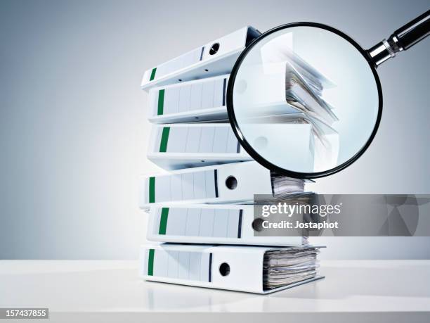 pile of binders partially obscured by a magnifying glass - lijst document stock pictures, royalty-free photos & images