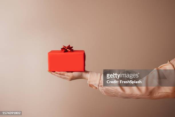 birthday surprise: a gift wrapped in an orange wrapping paper with a red bow ready to be delivered - wrapping arm stock pictures, royalty-free photos & images