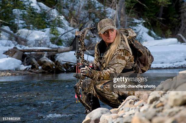 female hunter kneeling by a pile of rocks - archery bow stock pictures, royalty-free photos & images