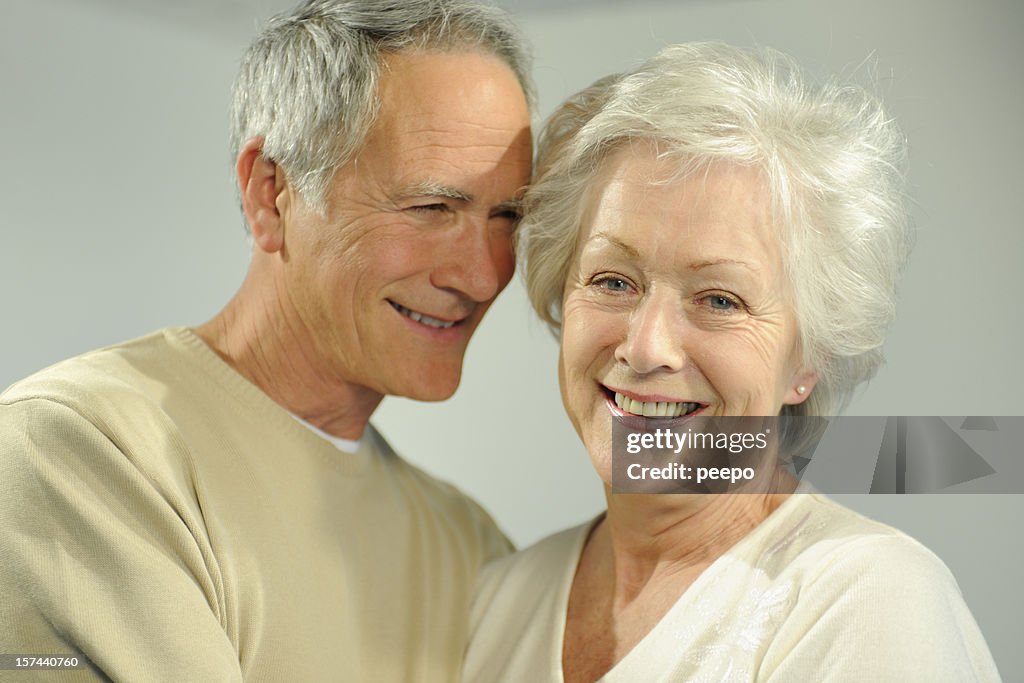 A senior couple smiles happily in a headshot.