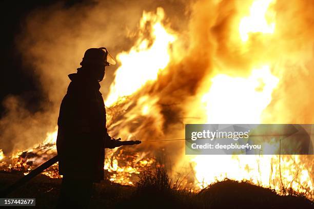 firefighter holding hose pointing water stream onto fire - brandweerman stockfoto's en -beelden