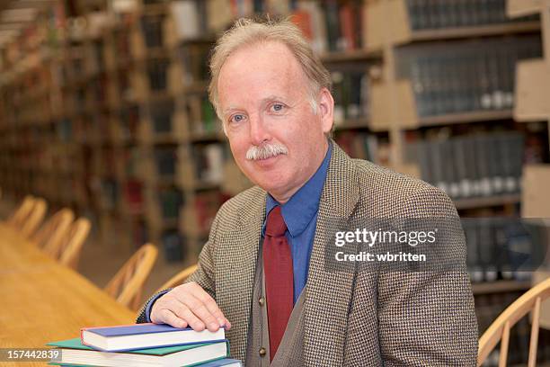 mature professor in a library holding some books - lecturer stock pictures, royalty-free photos & images