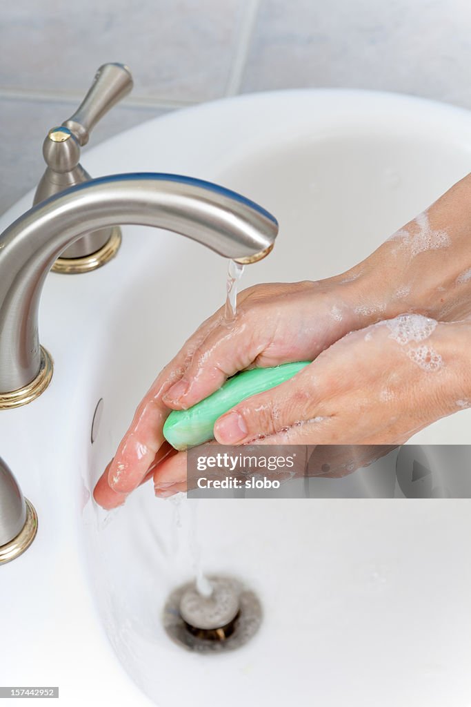 Adult washing their hands with a green bar of soap.