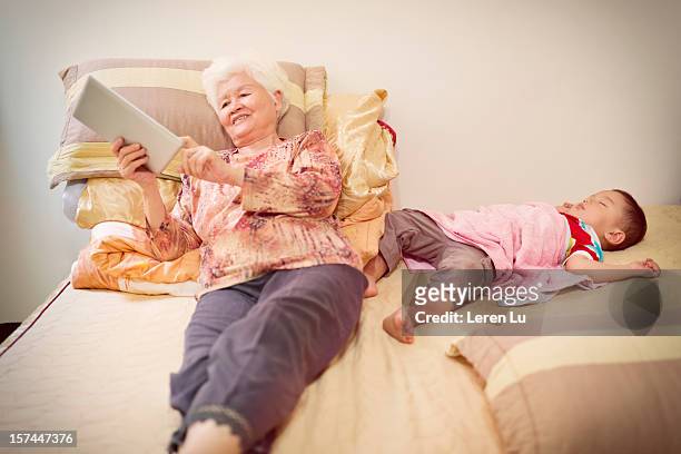 when child sleeping, grandmother is using a tablet - grandma sleeping stockfoto's en -beelden