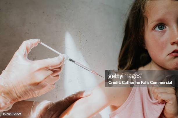 an unhappy little girl receives an injection in her arm - child punching stock pictures, royalty-free photos & images