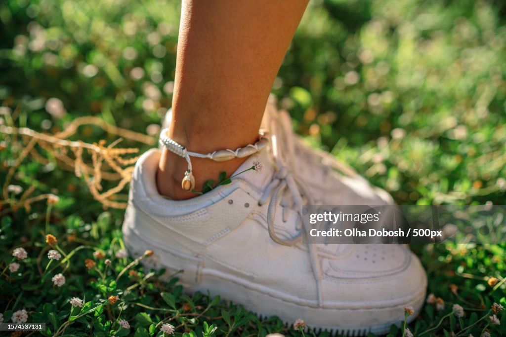 Low section close-up of girl wearing white shoes on grass field,Spain