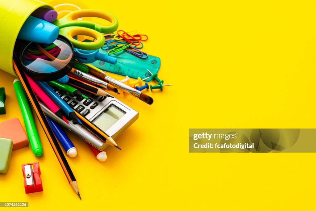 Close up view of a desk organizer full of school supplies laying on yellow background. Copy space