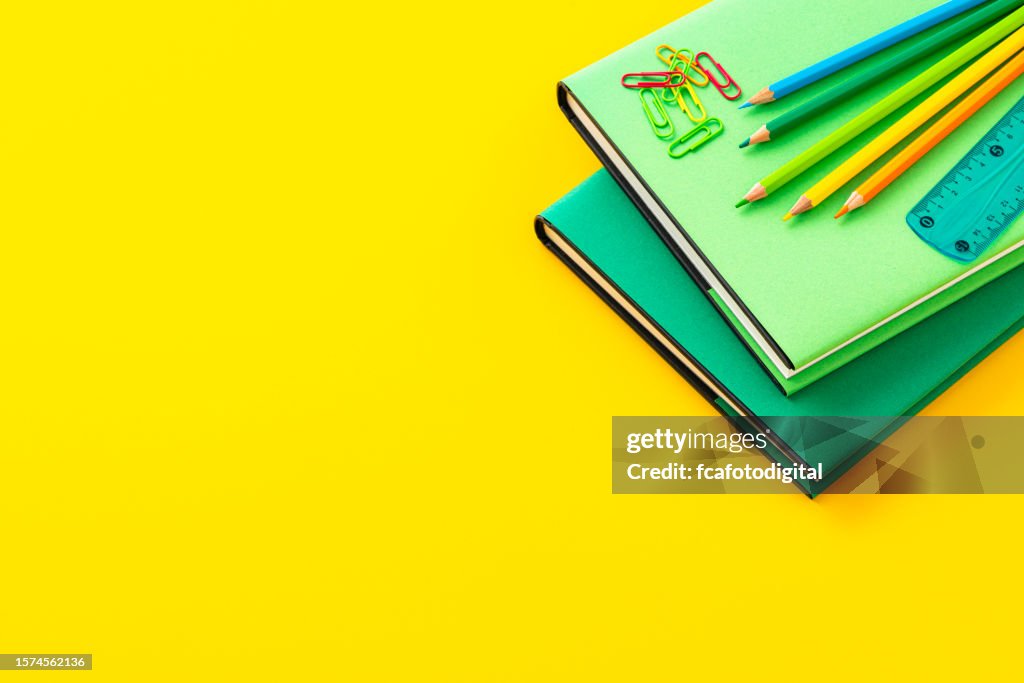 Books and crayons on yellow background with copy space