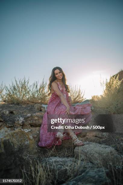 portrait of woman sitting on rock against sky,spain - fashion long dress stock pictures, royalty-free photos & images