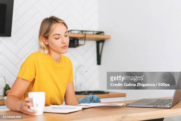 young woman working at laptop in kitchen at home,girl with cup of the morning coffee with papers - homegirl stock pictures, royalty-free photos & images