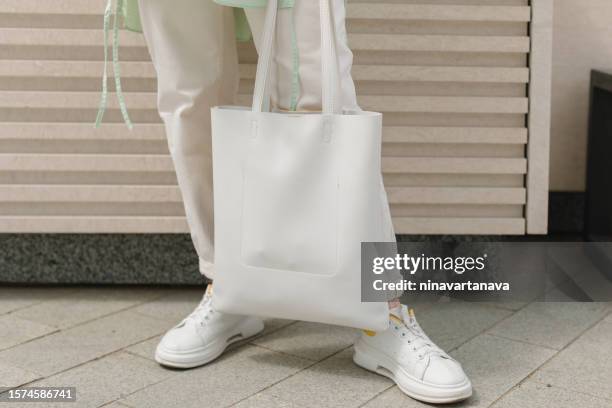 close-up low section view of a woman standing outdoors holding a plain white tote bag - sac fourre tout photos et images de collection