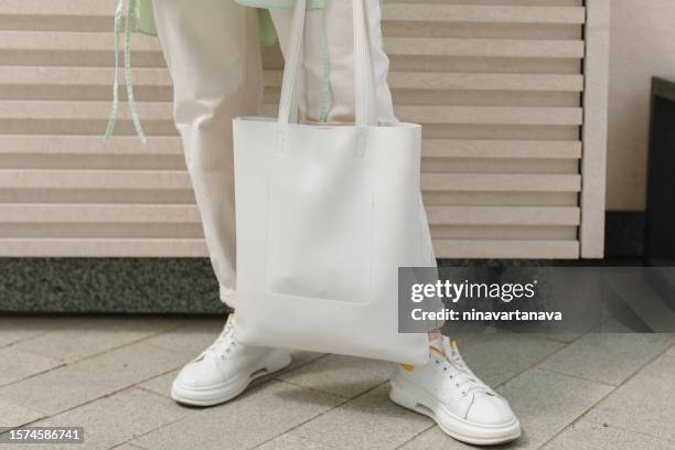 close-up low section view of a woman standing outdoors holding a plain white tote bag - tote bags stock pictures, royalty-free photos & images