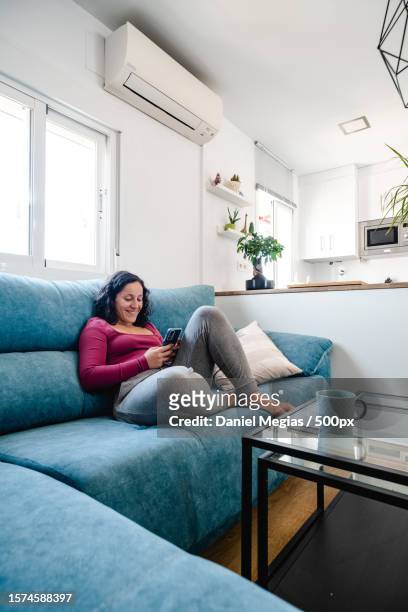 spanish woman texting with her cell phone sitting on the sofa,granada,spain - curled up reading stock pictures, royalty-free photos & images