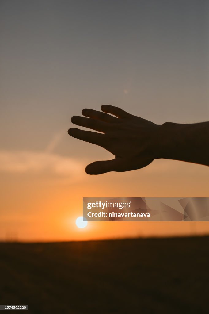 Silhouette of a man's hand reaching for the sun at sunset, Belarus