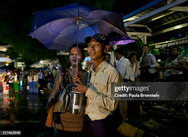 Burmese couple stands in the rain waiting at a bus stop November 30, 2012 in Yangon, Myanmar. Business is booming in this newly opened Southeast...