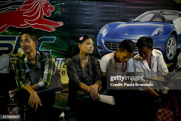 Burmese wait at a bus stop after work next to advertisements about new cars November 30, 2012 in Yangon, Myanmar. Business is booming in this newly...