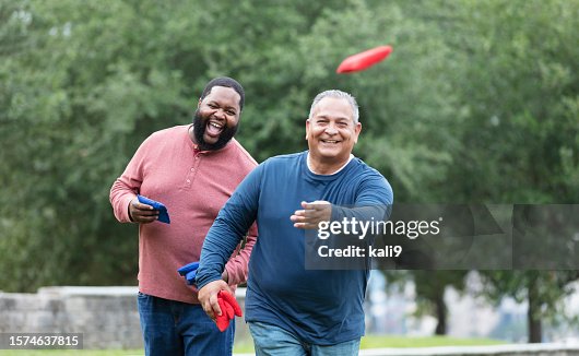 Two heavyset multiracial men playing bean bag toss Two heavyset multiracial men playing bean bag toss