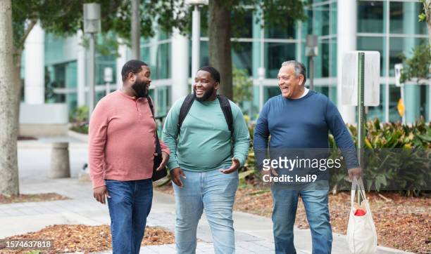 three heavyset multiracial men walking on city sidewalk - buildings side by side stock pictures, royalty-free photos & images