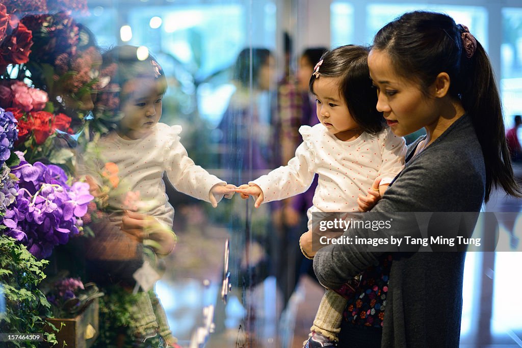 Mom carrying baby shopping for flowers in a mall