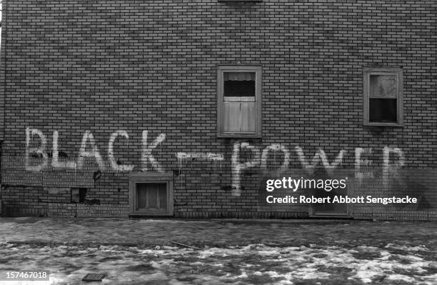 View of graffiti written on the shingled wall of an apartment building on an ice-covered sidewalk, in an unidentified part of Chicago, circa 1960s....