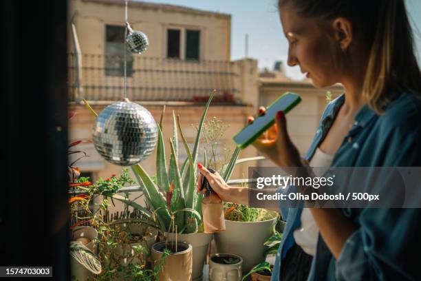 portrait of woman watering plans next to disco ball on outdoor balcony,spain - balkon blumen stock-fotos und bilder